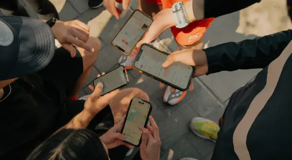Grupa biegaczy sprawdza swoje wyniki na telefonach. Widać mapy tras i statystyki aktywności, typowe dla aplikacji Strava po polsku.