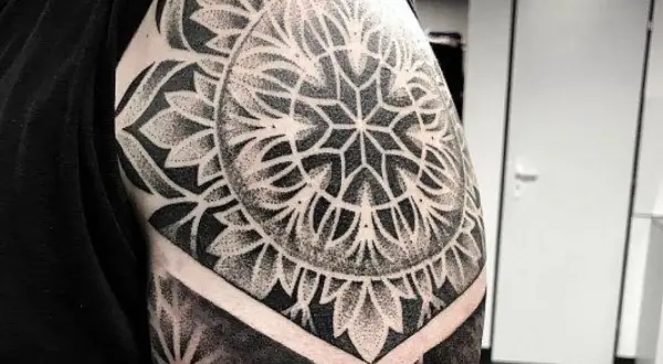 Imponujący tatuaż mandala na ramieniu, wykonany techniką dotwork. Wzór przypomina geometryczny kwiat, otoczony płatkami.