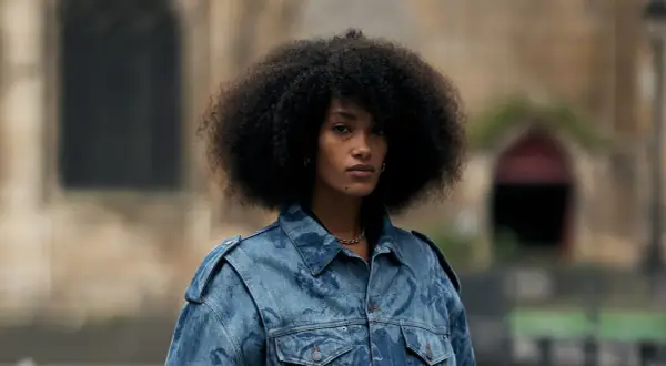 Frau mit Afro-Frisur trägt eine auffällige Jeansjacke, die perfekt zu einem lässigen Baggy Jeans Outfit passt.