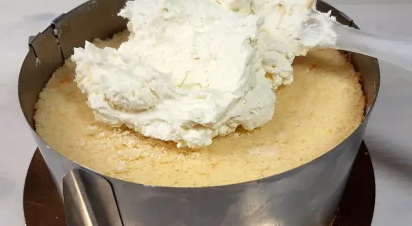 Nakładanie puszystej masy z mascarpone na biszkopt w tortownicy.
