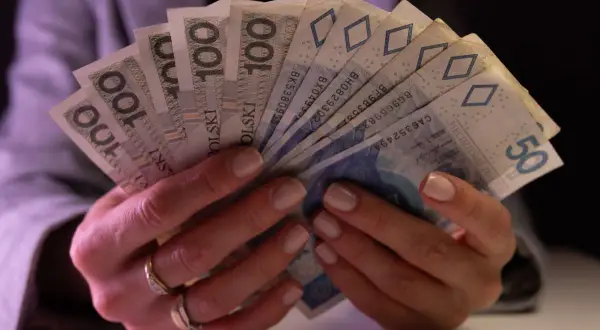Dłonie trzymające plik banknotów 100 zł i 50 zł. Taki jest koszt życia.