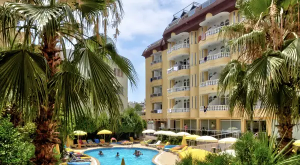 Basen z palmami i żółtym budynkiem hotelowym w tle.