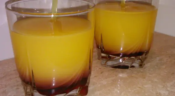 Dwa szklanki z żółtym drinkiem i ciemnym dnem, na marmurowym blacie.