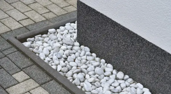 Grus runt huset med stenläggning och en mörk, strukturerad vägg.