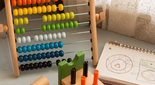 Ábaco de madera con cuentas de colores y un cuaderno con dibujos, ideales para ejercicios de atención y aprendizaje temprano.