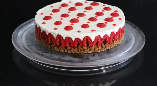 Cheesecake sans cuisson aux framboises, garni de points de coulis rouge sur une base croustillante.