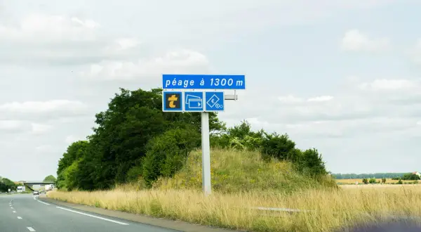 Panneau routier annonçant un péage à 1300m, avec symboles pour télépéage, cartes bancaires et espèces. La route Paris-Nantes se déroule sous un ciel nuageux.