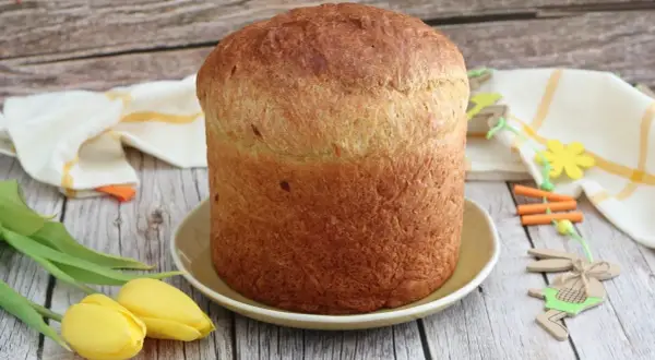 Gâteau de Pâques italien doré, prêt à être décoré d'œufs durs. Tulipes jaunes et décorations de lapin apportent une touche festive.
