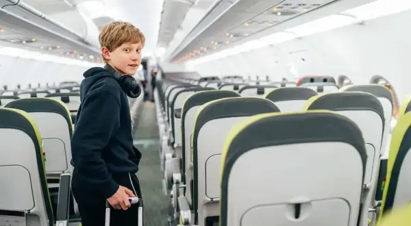 Chłopiec z walizką i słuchawkami na szyi w samolocie. Wizzair od ilu lat można latać samemu?