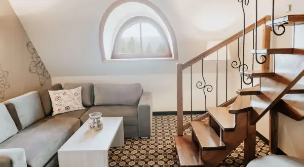 Przytulny salon z kanapą i stolikiem, drewniane schody i okno z widokiem na góry. Idealne miejsce na relaks i odkrywanie kocierz atrakcje.