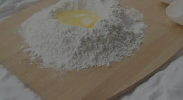 Mjöl och ett ägg ligger på en skärbräda, redo att blandas. Kanske för en kaka eller pannkakor, där bikarbonat och bakpulver kan komma till användning.