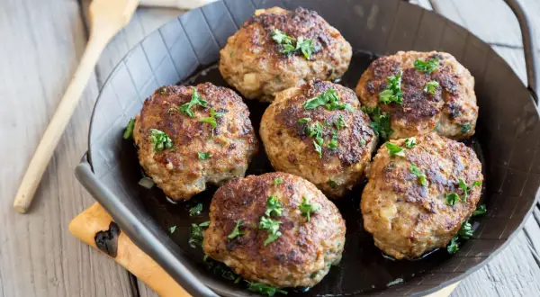 Sechs goldbraune Fleischpflanzerl, garniert mit Petersilie, in einer Pfanne. Ein leckeres Fleischpflanzerl Rezept zum Nachkochen.