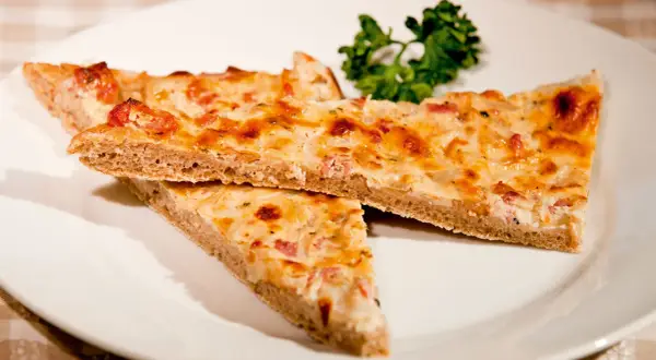Drei Stücke herzhafter Blooz mit Speck und Zwiebeln auf einem Teller, garniert mit Petersilie. Ein köstliches Blooz-Rezept.