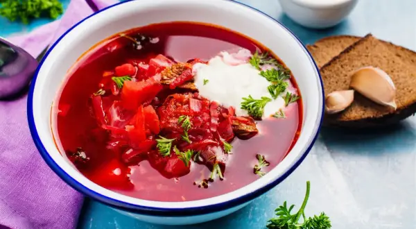 Gęsta, aromatyczna zupa z botwiny na mięsie, podana z kleksem śmietany i świeżą natką pietruszki. Obok kromki ciemnego chleba i ząbki czosnku.