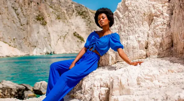 Modelka w niebieskim komplecie, idealna odpowiedź na pytanie: jaka bluzka do niebieskich spodni? Wakacyjny look na tle skalistej plaży.