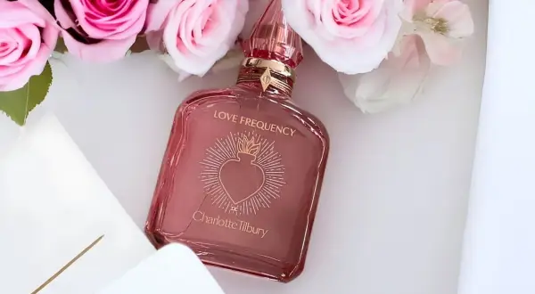 Różowe róże otaczają flakonik perfum Charlotte Tilbury Love Frequency.