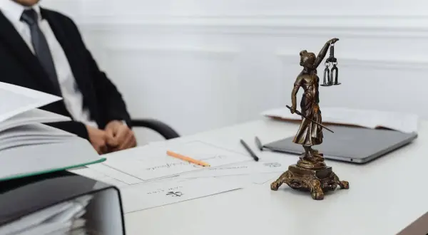 Prawnik omawia dyspozycję na wypadek śmierci w kilku bankach. Na biurku Statua Temidy, dokumenty i laptop.