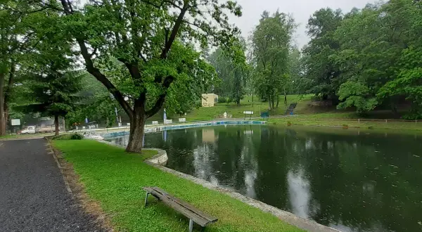 Spokojne stawy w Lądku-Zdroju, otoczone zielenią, zapraszają do odpoczynku. W oddali widać basen.