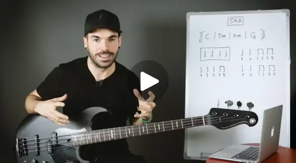 Hombre con bajo explica qué es el ska con un diagrama musical en una pizarra.