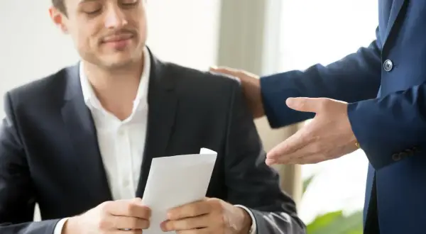 Mężczyzna w garniturze otrzymuje kopertę, być może wynagrodzenie za pracę bez umowy. Druga ręka kładzie się na jego ramieniu.