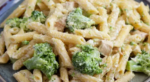 Penne z kurczakiem i kremowym sosem, w którym dominują zielone różyczki brokułów. Danie posypane startym parmezanem.