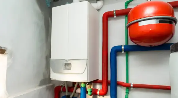 Montaż kotła gazowego w toku. Biały kocioł, czerwony zasobnik i kolorowe rury tworzą instalację grzewczą.