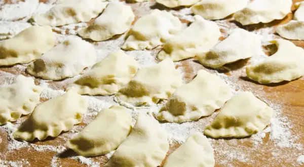 Surowe pierogi ułożone na drewnianej desce, posypane mąką.