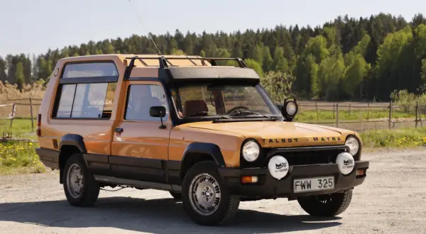 En orange Talbot Matra Rancho står parkerad på en grusväg med skog i bakgrunden.