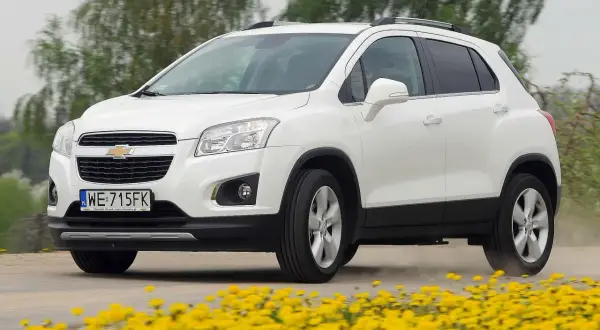 Biały Chevrolet Trax jedzie po drodze, otoczony żółtymi kwiatami.