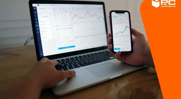 Persona usando un portátil y un móvil para conectar movil a pc y ver gráficos financieros.