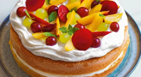 Torta compleanno pan di spagna con panna montata e frutta fresca: pesche, uva rossa e bianca, prugne e foglioline di menta.