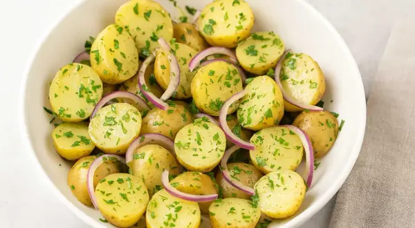 En skål med fransk potatissallad, full av små, kokta potatisar, rödlök och färsk persilja.