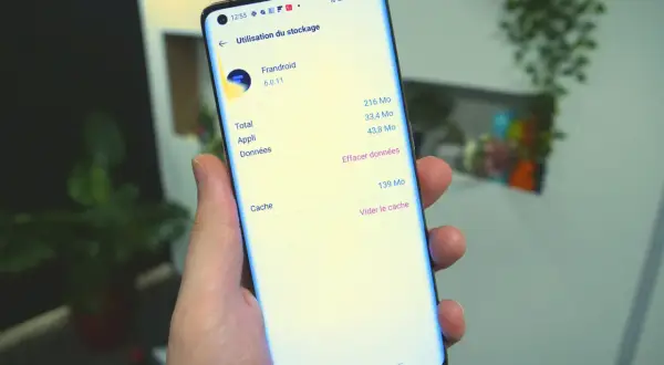 Une main tient un smartphone affichant l'option "Vider le cache" pour l'application Frandroid.