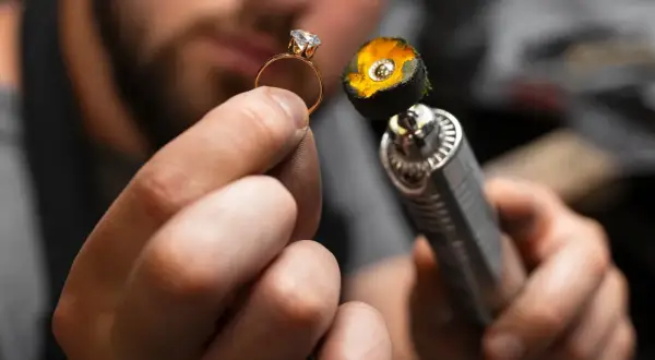 Manos de joyero puliendo un anillo de oro con un diamante. La herramienta de pulido tiene una placa de oro en su extremo.