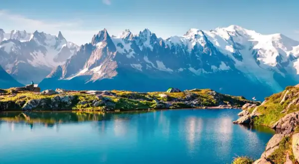 Lac alpin paisible reflétant les sommets enneigés du Mont-Blanc. Un campement discret et un randonneur contemplent ce paysage grandiose, parfait pour une randonnée tour du mont blanc.