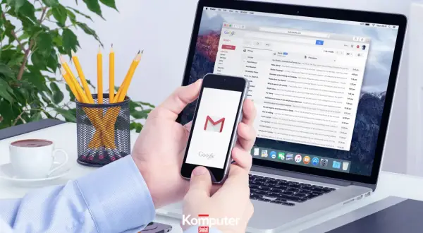 Ręce trzymają smartfon z ikoną Gmail, obok laptop z otwartą pocztą. Jak się wylogować z konta Google?