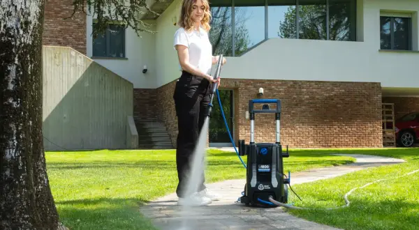 Donna usa idropulitrice per pulire il sentiero di cemento, mostrando come togliere il muschio.