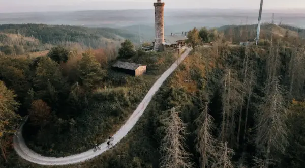 Radfahrer auf einem Weg zum Aussichtsturm Bergneustadt. Der Turm thront über einer bewaldeten Hügellandschaft.