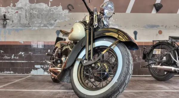 Klasyczny motocykl z białymi bokami opon, stojący w garażu.