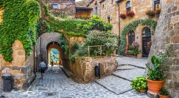 Un vicolo acciottolato tra antichi edifici ricoperti di edera e fiori, un invito a scoprire i borghi da visitare nelle Marche.