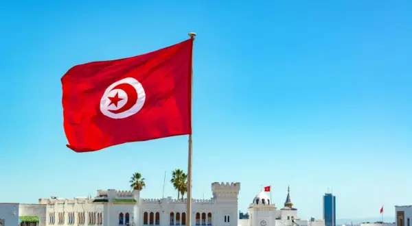 Tunisiens flagga vajar stolt mot en klarblå himmel över vita byggnader. En påminnelse om en resa till Tunisien.
