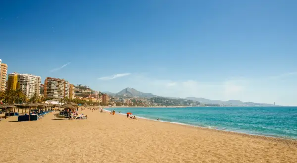 Playa con sombrillas y tumbonas, gente disfrutando del sol y el mar. ¡Unas de las mejores playas cerca de Madrid!