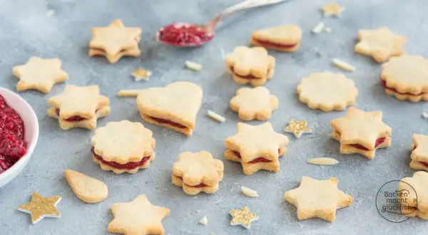 Sterne und Herzen aus veganen Keksen mit Marmeladenfüllung, dekoriert mit glitzernden Sternen.