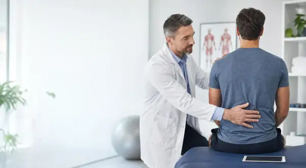 Medico esamina la schiena di un paziente, illustrando la differenza tra fisiatra e ortopedico.
