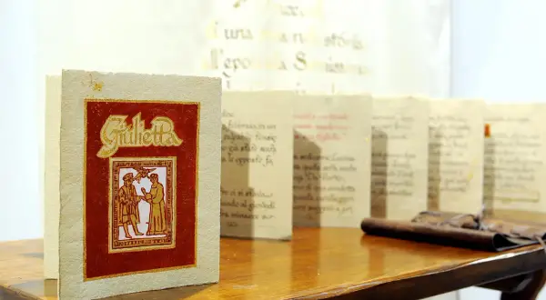 Libri con copertina rossa e dorata, "Giulietta", e altri volumi con testo calligrafico, esempi di prodotti artigianali Friuli Venezia Giulia.