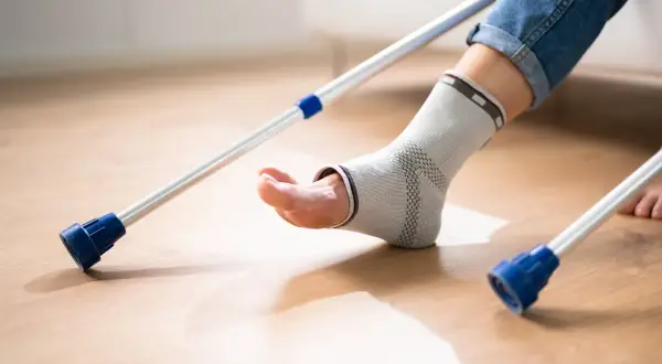 Osoba w ortezie na stawie skokowym próbuje chodzić z kulami. Rehabilitacja po artrodezie stawu skokowego wymaga cierpliwości.