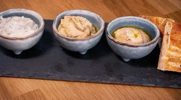 Tre skålar med dipp, en med dill, och två med en smak av 7 kryddor, serveras med rostat bröd på en stenplatta.