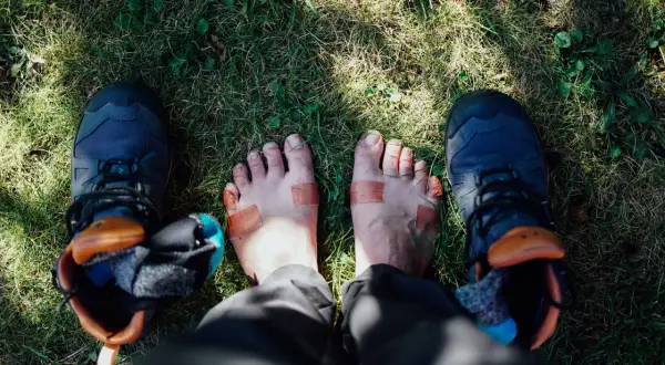 Fötter med plåster och vandringsskor på gräs. Kanske dags för nya vandringsstrumpor sommar?