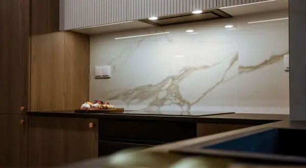 Elegancka kuchnia z drewnianymi frontami i płytkami z subtelnym marmur wzór. Na blacie deska z warzywami.
