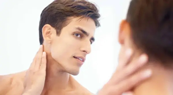 Un homme au visage fin et à la mâchoire marquée, la main caressant son cou, révélant une belle v line.